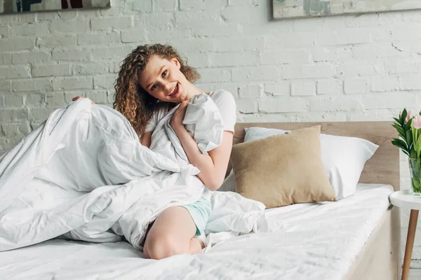 Attractive cheerful girl in homewear sitting on bed in morning — Stock Photo