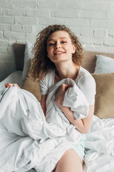 Glückliches attraktives Mädchen in Homewear sitzt morgens auf dem Bett — Stockfoto