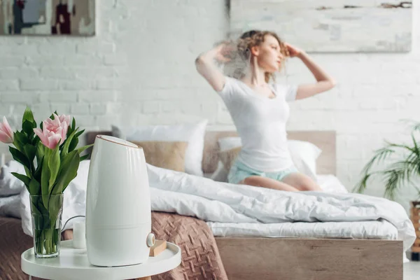 Selektiver Fokus des Mädchens im Schlafzimmer mit Tulpenblüten und Luftreiniger, der Dampf verbreitet — Stockfoto