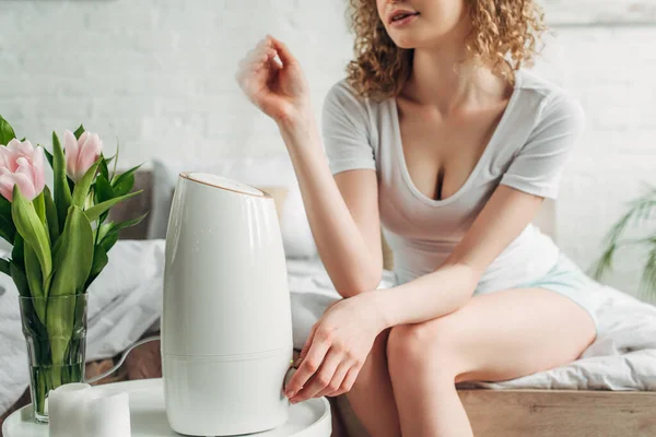 Cropped view of girl sitting in bedroom with air purifier and tulip flowers — Stock Photo