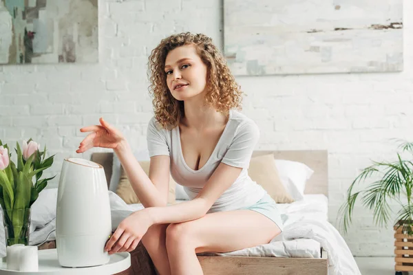 Hermosa chica sonriente sentada en el dormitorio con purificador de aire y tulipanes — Stock Photo