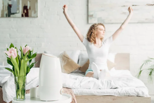 Enfoque selectivo de chica feliz estiramiento en el dormitorio con purificador de aire y tulipanes — Stock Photo