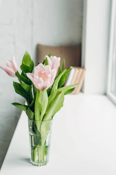 Bouquet of pink tulip flowers in glass on windowsill with books — Stock Photo