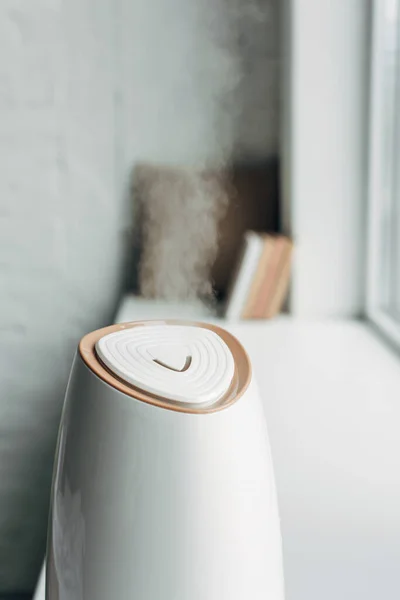 Humidifier spreading steam and standing on windowsill at home — Stock Photo