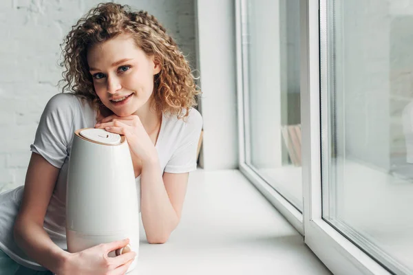 Jolie fille souriante avec purificateur d'air sur le rebord de la fenêtre — Photo de stock