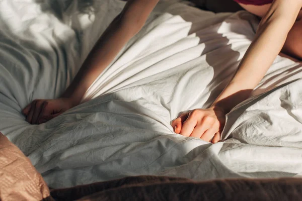 Обрезанный вид на девушку на кровати в спальне с солнечным светом и тенями — стоковое фото