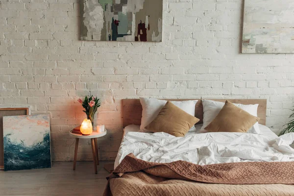 Интерьер спальни с кроватью, гималайская соляная лампа, тюльпаны и картины — стоковое фото