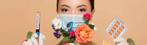 Panoramic shot of asian girl in latex gloves and floral face mask with butterfly holding pills and coronavirus blood test isolated on beige — Stock Photo