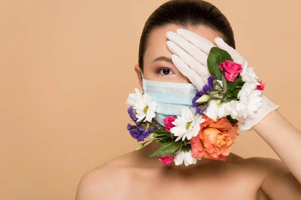 Beautiful naked asian girl in latex gloves and floral face mask closing eye isolated on beige — Stock Photo