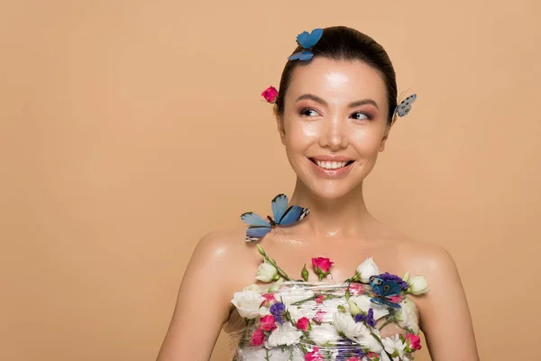 Atractivo sonriente chica asiática desnuda en flores con mariposas en el cuerpo aislado en beige - foto de stock