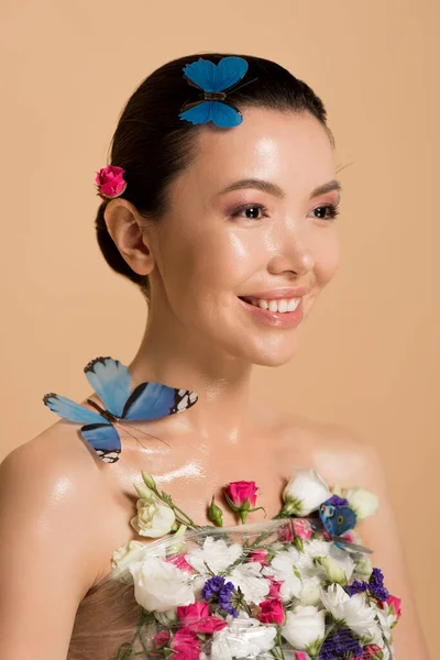 Smiling naked asian girl in flowers with butterflies on body isolated on beige — Stock Photo