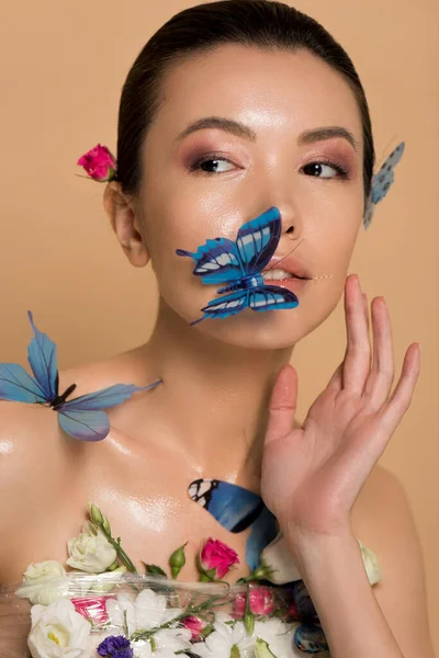 Красива оголена азіатська дівчина в квітах з метеликами на тілі ізольована на бежевому — стокове фото