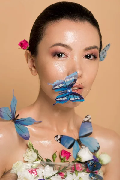 Приваблива ніжна гола азіатська дівчина в квітах з метеликами на обличчі ізольована на бежевому — стокове фото