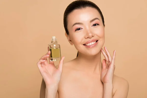 Attractive cheerful nude asian girl applying oil on face isolated on beige — Stock Photo