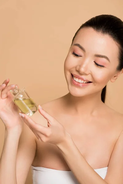 Attractive smiling asian girl holding bottle of oil on beige — Stock Photo