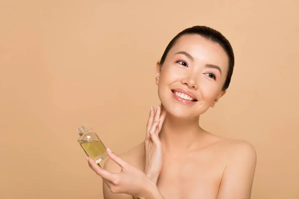 Beautiful smiling naked asian girl applying perfume on skin isolated on beige — Stock Photo