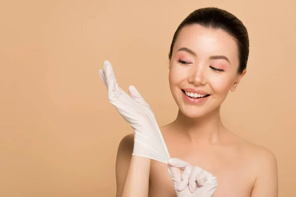 Attractive happy naked asian girl in latex gloves isolated on beige — Stock Photo