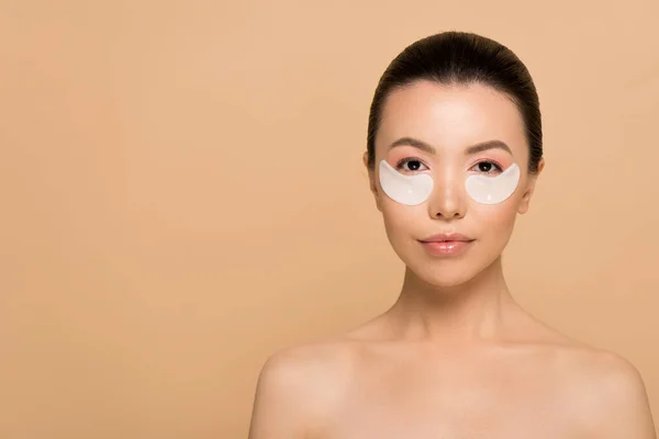 Atractivo desnudo asiático mujer con colágeno ojo almohadillas aislado en beige - foto de stock