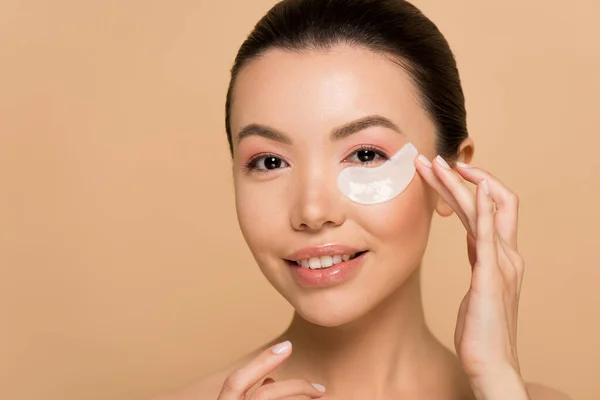 Bella sorridente asiatico ragazza con collagene occhio pad isolato su beige — Foto stock