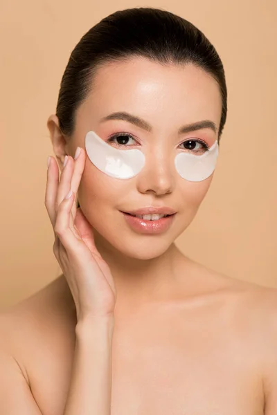 Tender nude asian girl with white collagen eye pads isolated on beige — Stock Photo