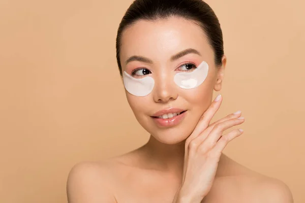 Beautiful tender nude asian girl with collagen eye pads isolated on beige — Stock Photo