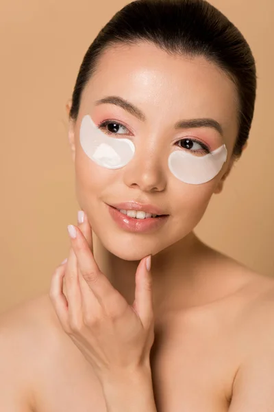 Atractivo tierno desnudo asiático chica con colágeno ojo almohadillas aislado en beige - foto de stock