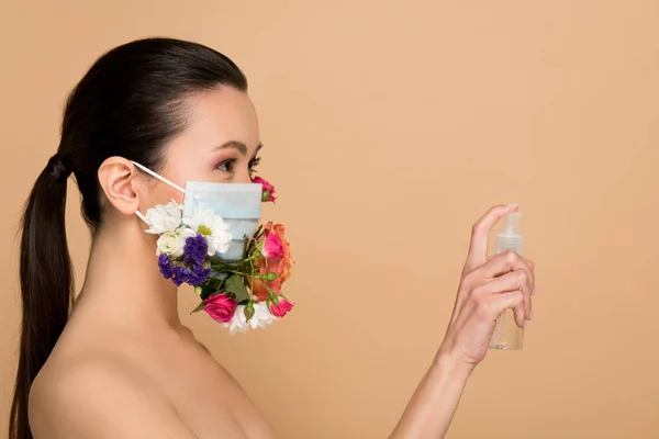 Atraente nu ásia menina no floral rosto máscara segurando antisséptico spray isolado no bege — Fotografia de Stock