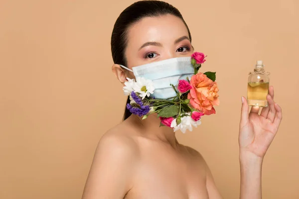 Attractive nude asian girl in floral face mask holding glass bottle of perfume isolated on beige — Stock Photo