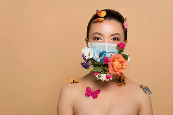 Hermosa mujer asiática en máscara facial floral con mariposas aisladas en beige - foto de stock