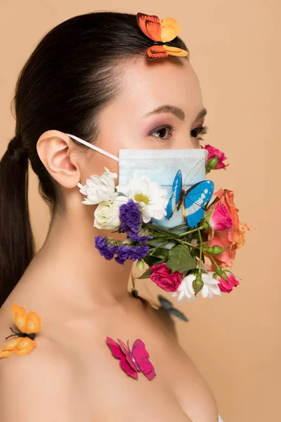 Atractiva mujer asiática en máscara facial floral con mariposas aisladas en beige - foto de stock