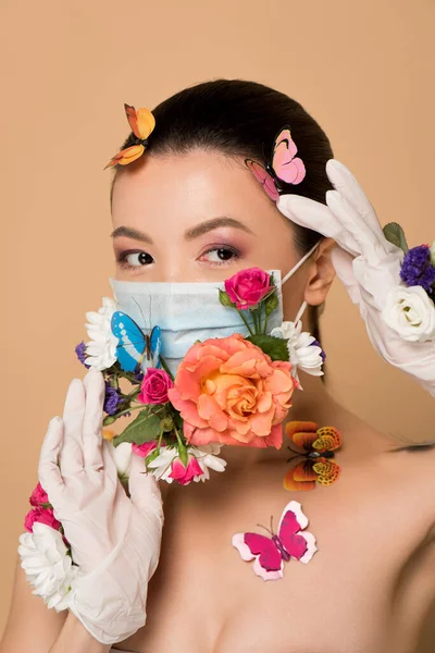 Schöne asiatische Frau in Latex-Handschuhen und floraler Gesichtsmaske mit Schmetterlingen auf beige — Stockfoto