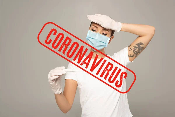 Mujer con máscara médica en guantes de látex sosteniendo termómetro y tocando la frente aislada en gris, ilustración coronavirus - foto de stock