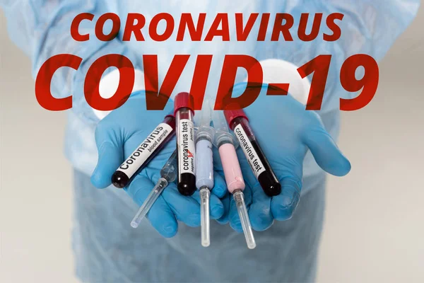 Cropped view of doctor holding test tubes with blood samples and coronavirus lettering and syringes isolated on grey, coronavirus covid-19 illustration — Stock Photo