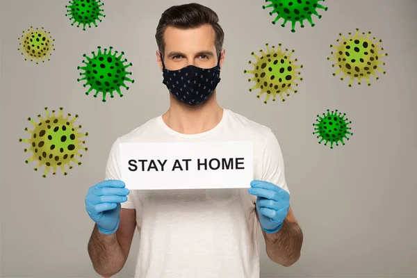 Man in safety mask and latex gloves holding card with stay at home lettering isolated on grey, bacteria illustration — Stock Photo