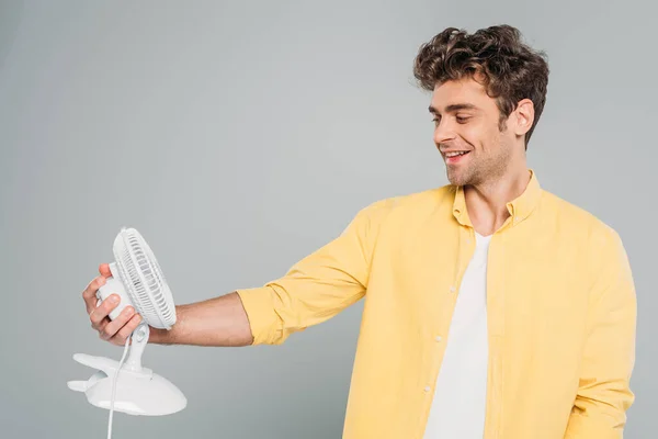 Mann lächelt und schaut Tischventilator isoliert auf grau — Stockfoto