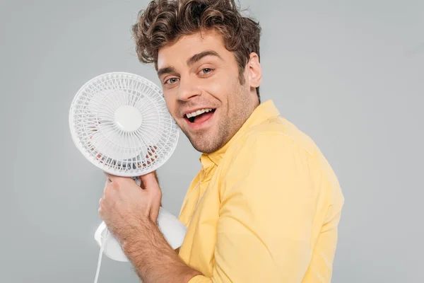 Uomo felice che tiene ventilatore scrivania, sorridente e guardando la fotocamera isolata su grigio — Foto stock