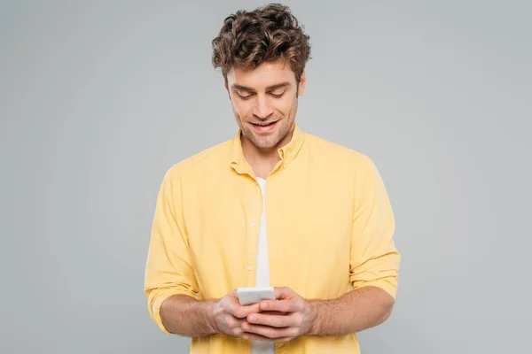 Vista frontal del hombre sonriendo y charlando en el teléfono inteligente aislado en gris - foto de stock