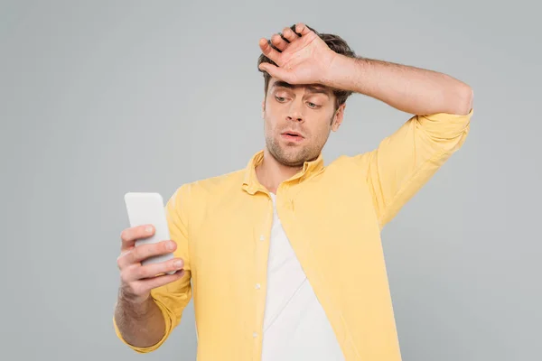 Вид спереди мужчины с поднятой рукой, смотрящего на смартфон, изолированный на сером фоне — стоковое фото