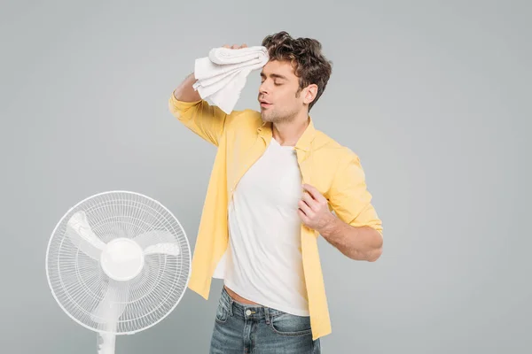 Uomo con asciugamano vicino ventilatore elettrico isolato su grigio — Foto stock