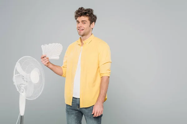 Homme aux ventilateurs électriques et manuels souriant et regardant la caméra isolée sur gris — Photo de stock