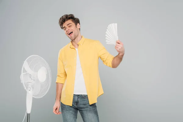 Homme excité avec ventilateurs électriques et manuels souriant et regardant la caméra isolée sur gris — Photo de stock