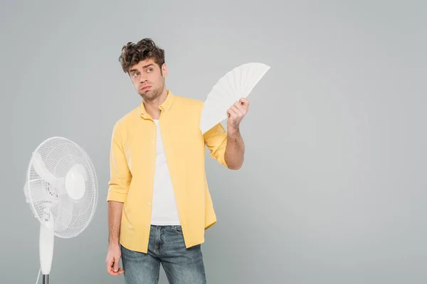 Uomo con ventilatori elettrici e a mano che distoglie lo sguardo isolato sul grigio — Foto stock