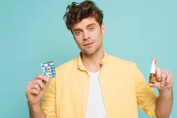 Vue de face de l'homme regardant la caméra et montrant bouteille de gouttes nasales et blister pack avec des pilules isolées sur bleu — Photo de stock