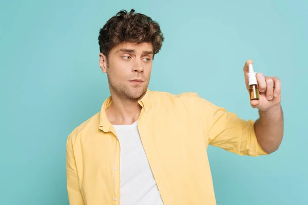 Homme regardant bouteille de gouttes nasales isolées sur bleu — Photo de stock