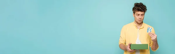 Vorderseite des Mannes mit Blisterverpackung mit Pillen und Schachtel mit Servietten isoliert auf blauem Grund, Panoramaaufnahme — Stockfoto