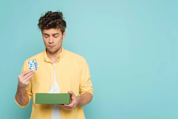 Vorderseite des Mannes mit Blisterverpackung mit Pillen und Schachtel mit Servietten isoliert auf blau — Stockfoto