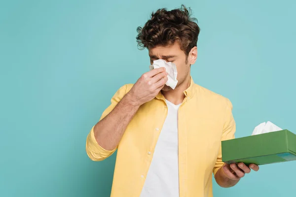 Man holding box with napkins and blowing out nose isolated on blue — Stock Photo