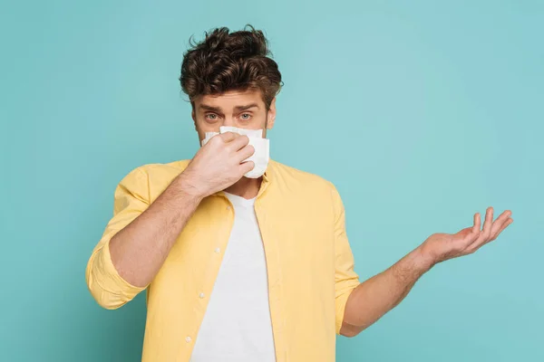 Vorderansicht eines Mannes, der mit Serviette die Nase auspustet, mit der Hand zeigt und isoliert auf blauem Grund in die Kamera blickt — Stockfoto