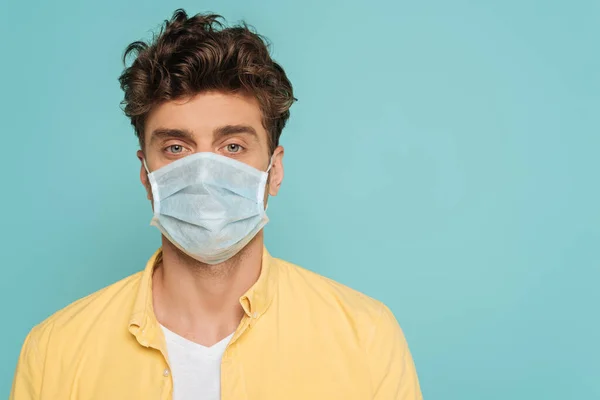 Портрет человека в медицинской маске, смотрящего на камеру, изолированную на голубом — стоковое фото