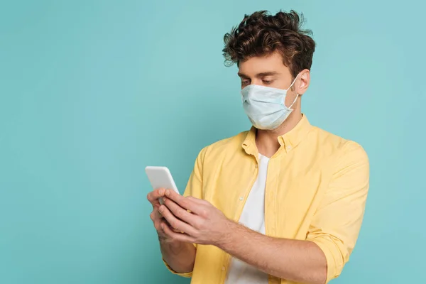 Concentrated man in medical mask typing on smartphone isolated on blue — Stock Photo